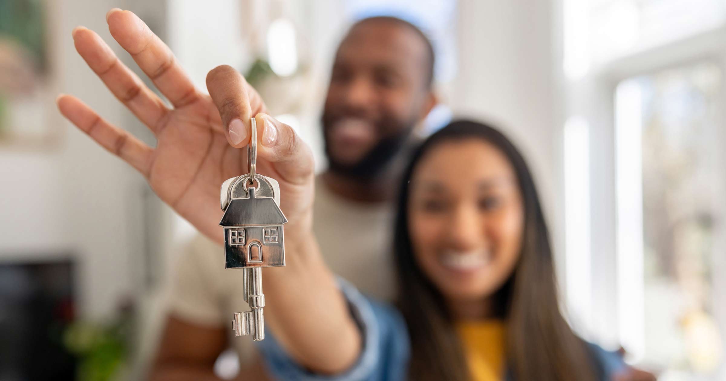 a blurry image of a woman and a man holding the house shaped key to a new house