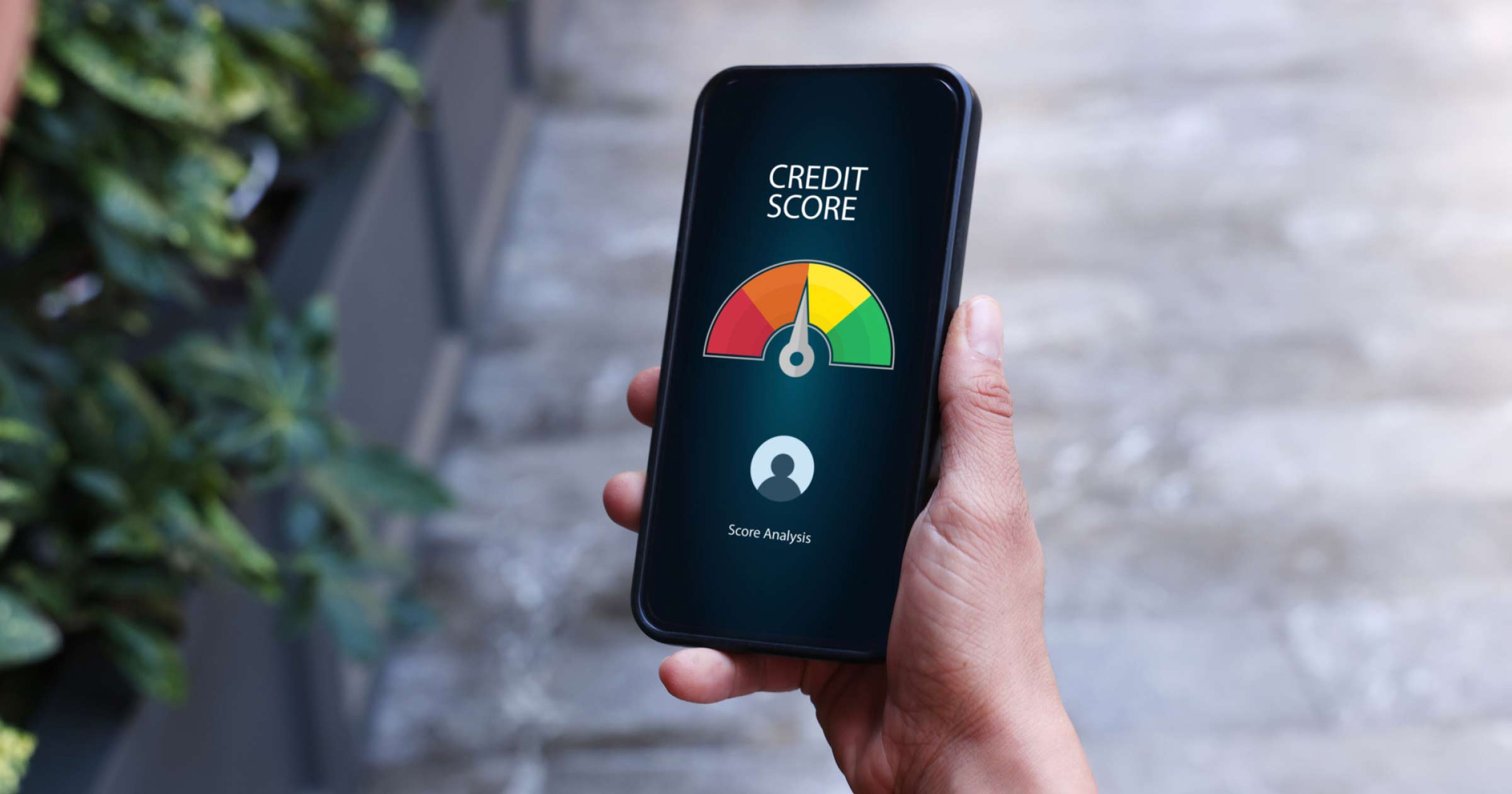 a picture of a smartphone in a person's hand with the word credit score above a scale from red to green, with the arrow in the middle between orange and yellow